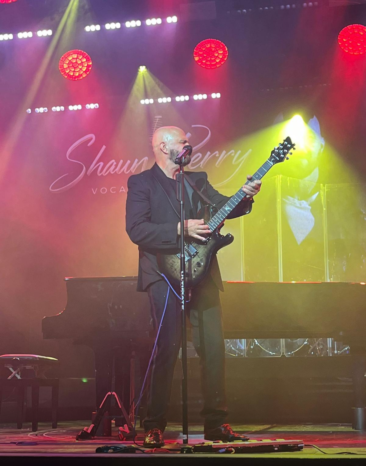 Shaun Perry performing live with his guitar under red and gold stage lighting