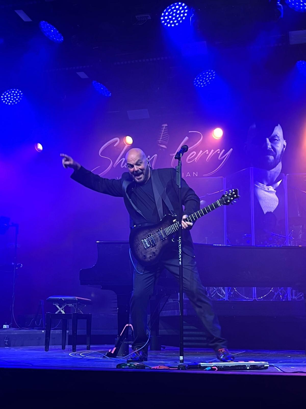 Shaun Perry entertaining the audience under blue stage lighting