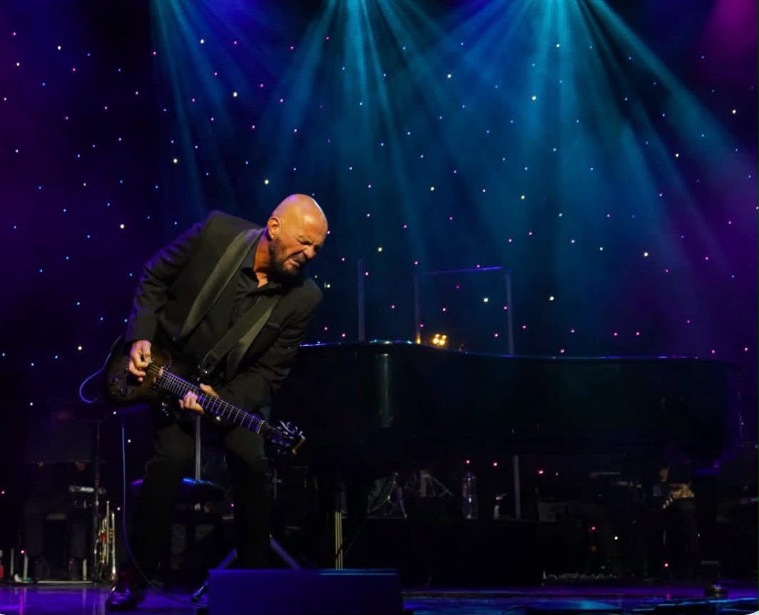 Shaun Perry performing a guitar solo beside a grand piano