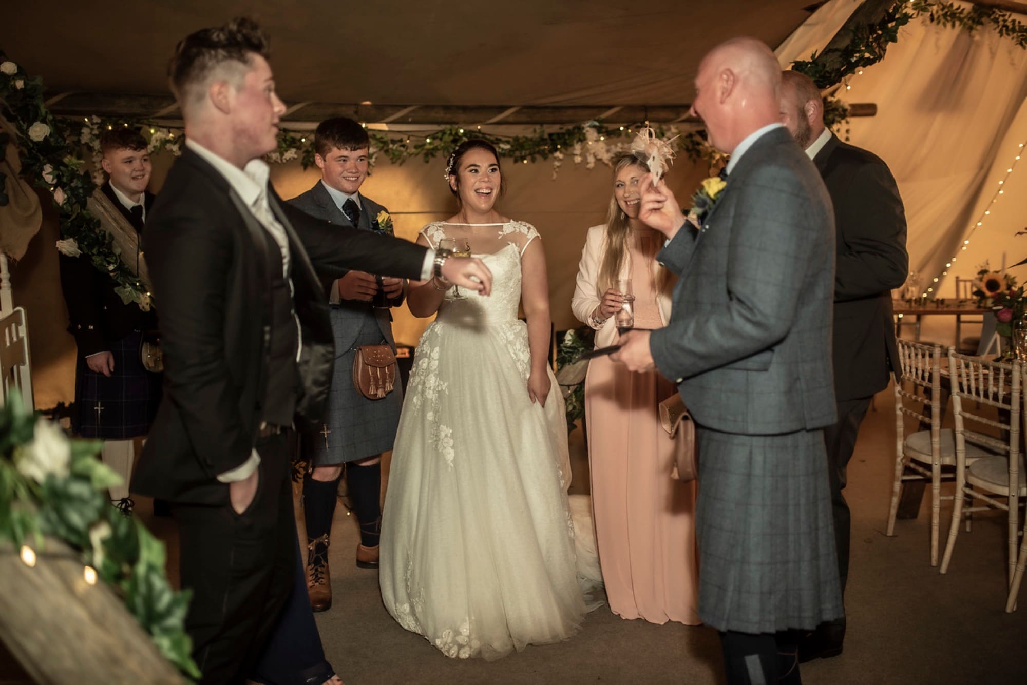 A bride and her guests mid-laugh as a playing card floats between them at a wedding reception