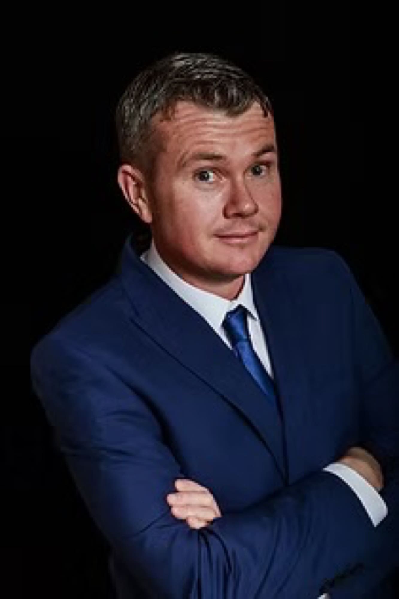 Portrait of a performer in a blue suit against a dark stage backdrop